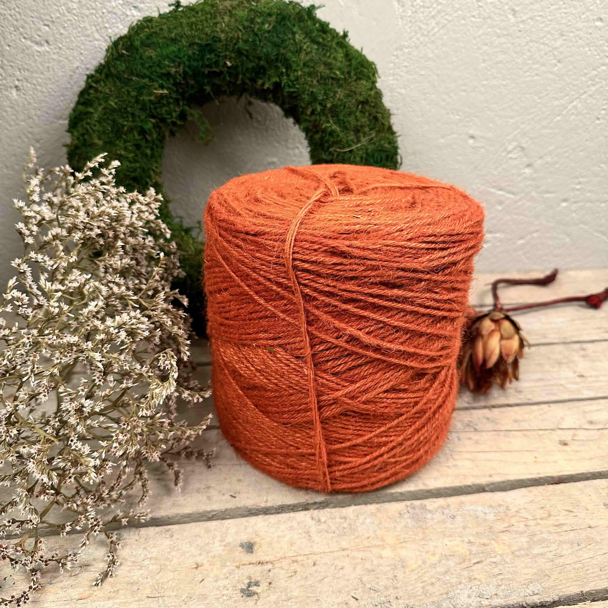 Orange jutesnöre på rulle framför mosskrans och torkade blommor