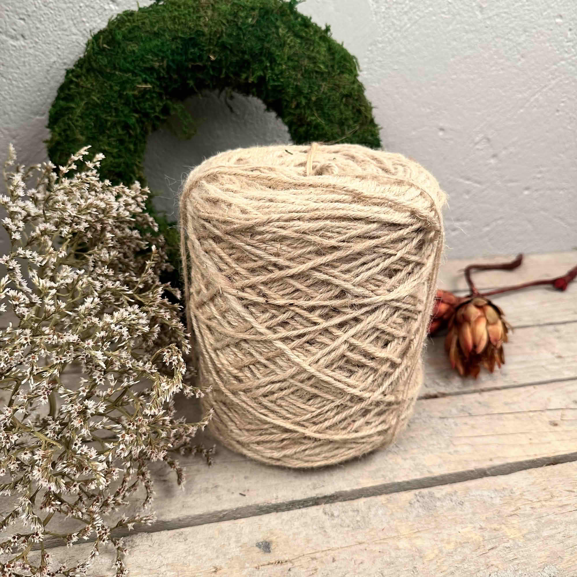Ljust naturfärgad jutesnörerulle framför grön mosskrans och torkade blommor